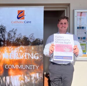 CatholicCare Wilcannia-Forbes team member Dylan Biles holds a poster for the organisation's Forbes Community Movie Night outside the branch office in Lachlan Street.